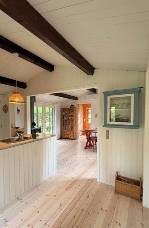 A spacious kitchen with a wooden floor, a dining area with red chairs, and a view through a doorway to a living room. - Bright holiday home with large garden, near beach (Nykøbing Sjælland)