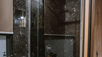 A modern bathroom with a glass shower enclosure, a white sink, and a dark marble wall.