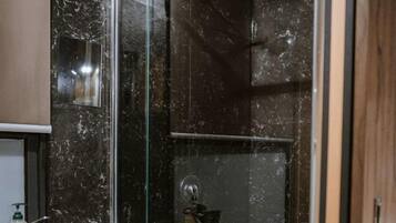 A modern bathroom with a glass shower enclosure, a white sink, and a dark marble wall.