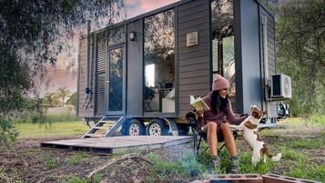 Una casa móvil moderna con una terraza, un hogar para fogata y una persona leyendo un libro.