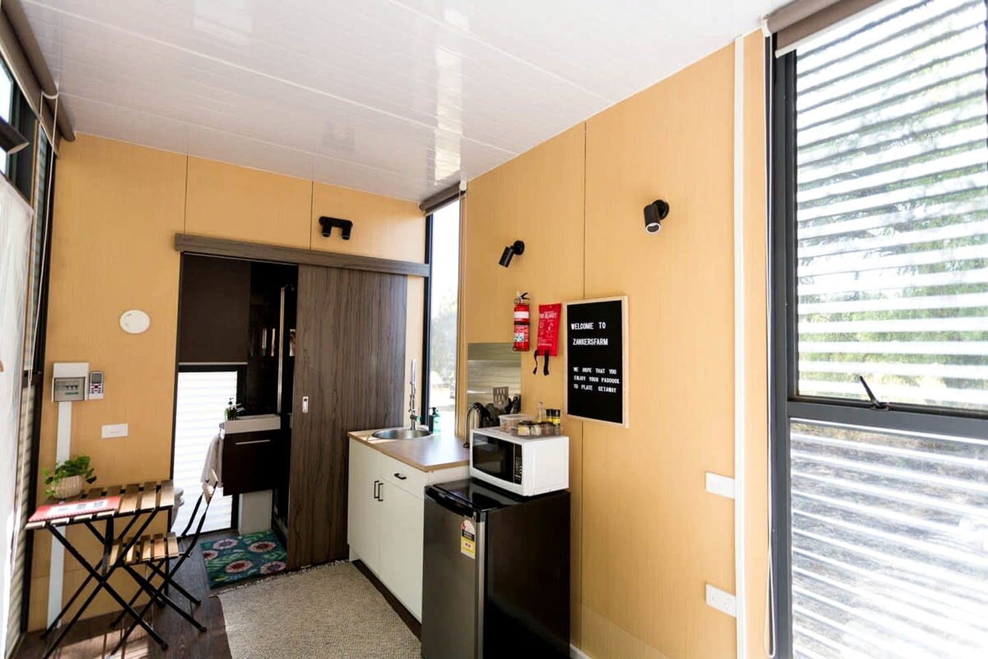 Eine kleine Küche mit Spüle, Herd und Kühlschrank, ein Essbereich mit Tisch und Stühlen sowie ein Fenster mit Jalousien.