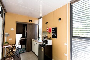 A compact kitchen with a sink, stove, and refrigerator, a small dining area with a table and chairs, and a window with blinds.