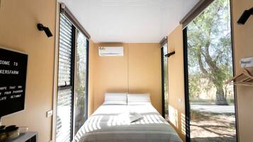 Una habitación pequeña con una cama, aire acondicionado en la pared y un cartel con texto.