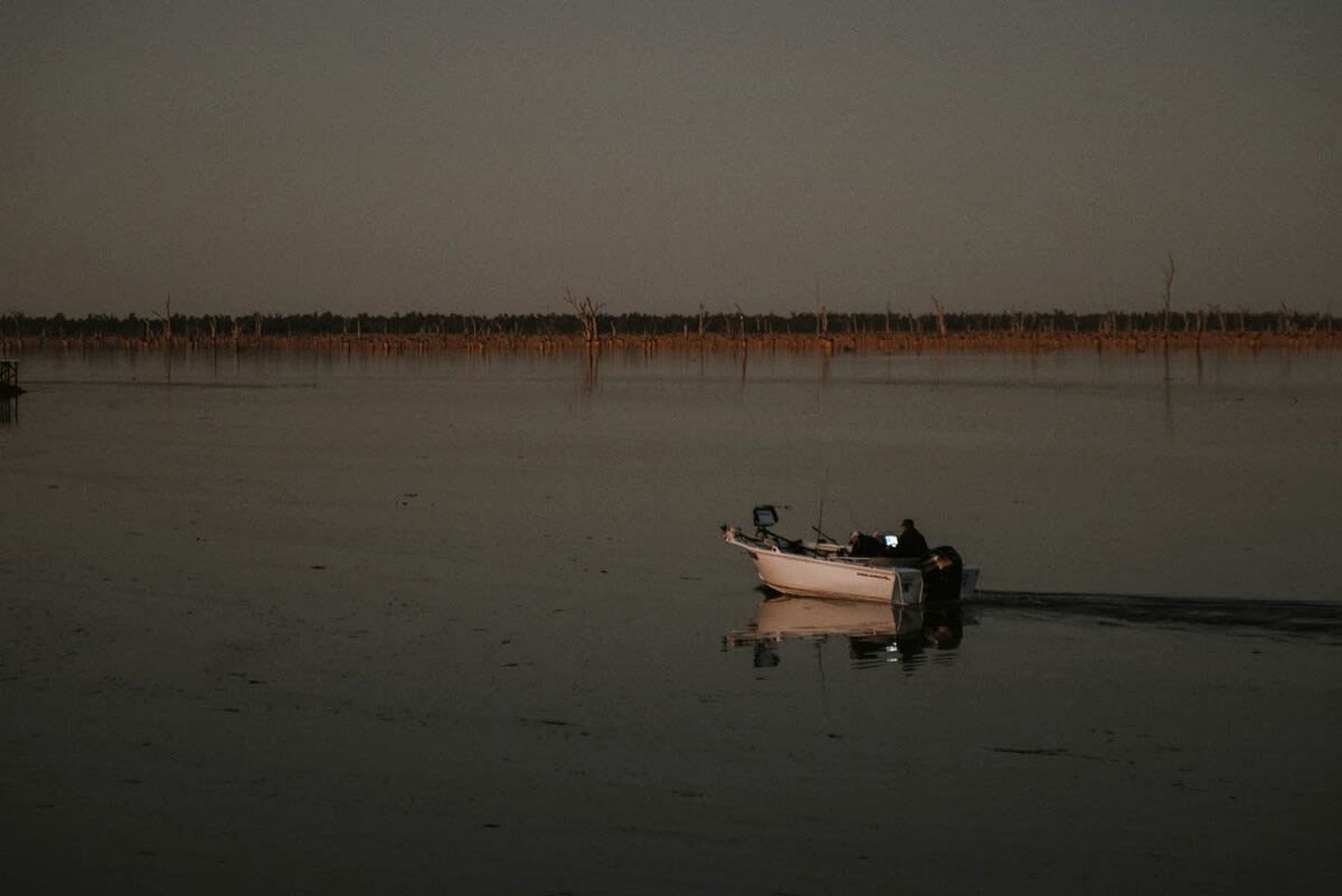A boat on a calm body of water with a flat horizon and sparse vegetation in the distance.