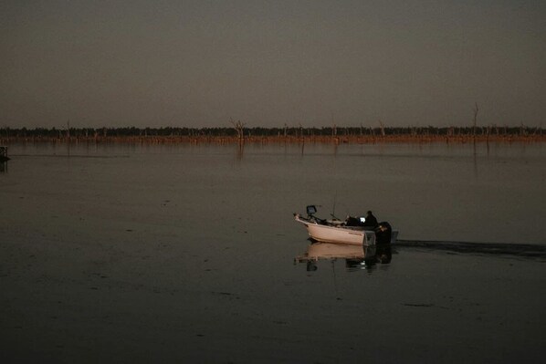A boat on a calm body of water with a flat horizon and sparse vegetation in the distance.