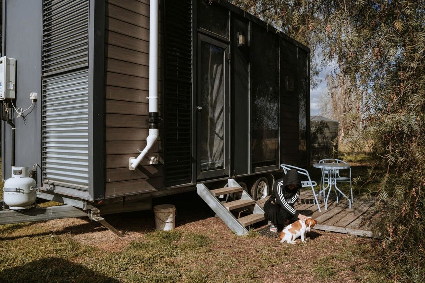 A mobile home with a porch, a gas tank, and a dog.