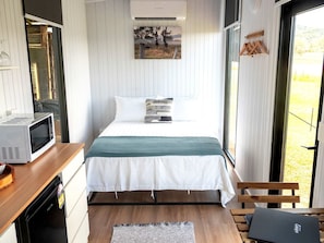 A bedroom with a bed, a microwave, a wooden desk, and a bench.