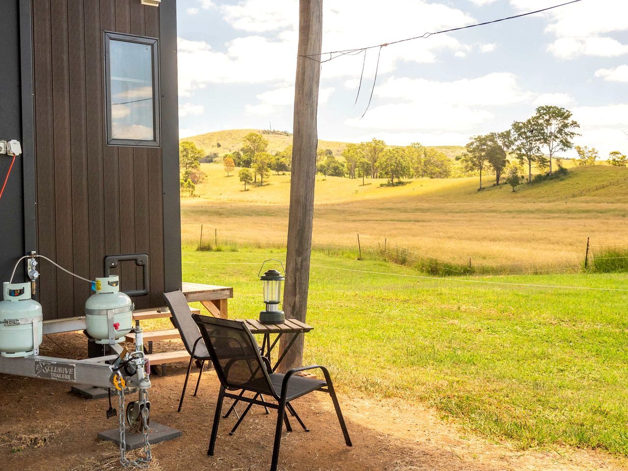 A rustic cabin with a wooden exterior, a table with chairs, propane tanks, and a lantern outside.