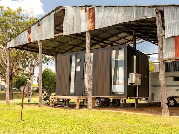 A mobile home with a metal roof, a small attached structure, and a table with chairs outside.