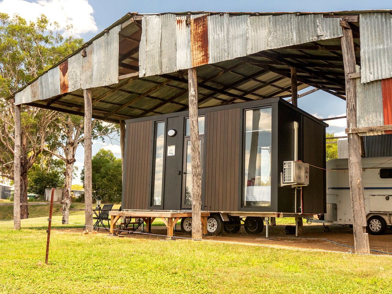 A mobile home with a metal roof, a small attached structure, and a table with chairs outside.