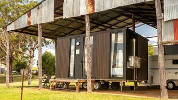 A mobile home with a metal roof, a small attached structure, and a table with chairs outside.