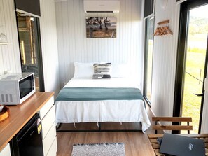 Un dormitorio con una cama, un microondas, un escritorio de madera y un banco.