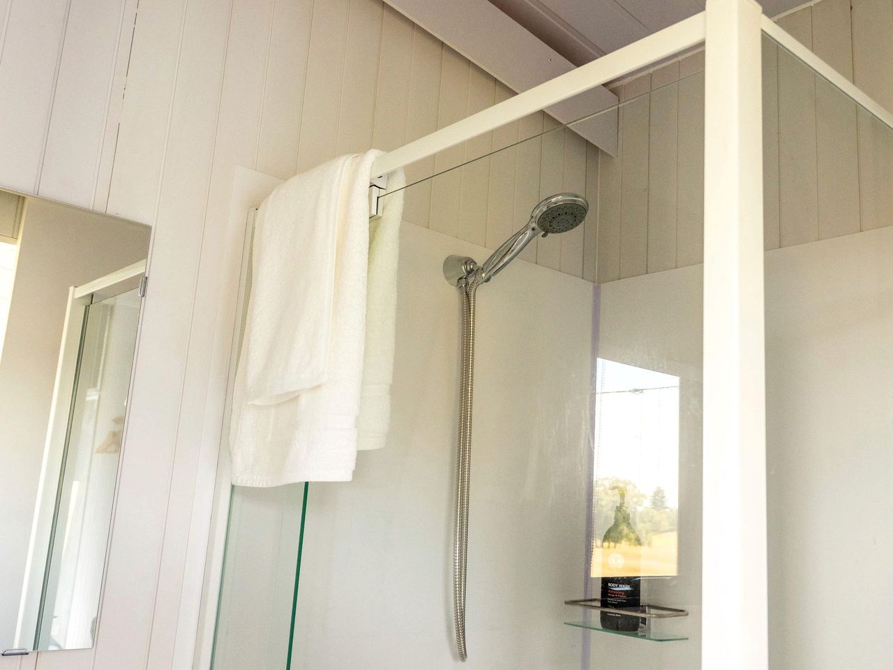 Une douche équipée d’un pommeau de douche à main, une serviette suspendue à un porte-serviettes et un lavabo en verre avec un distributeur de savon.