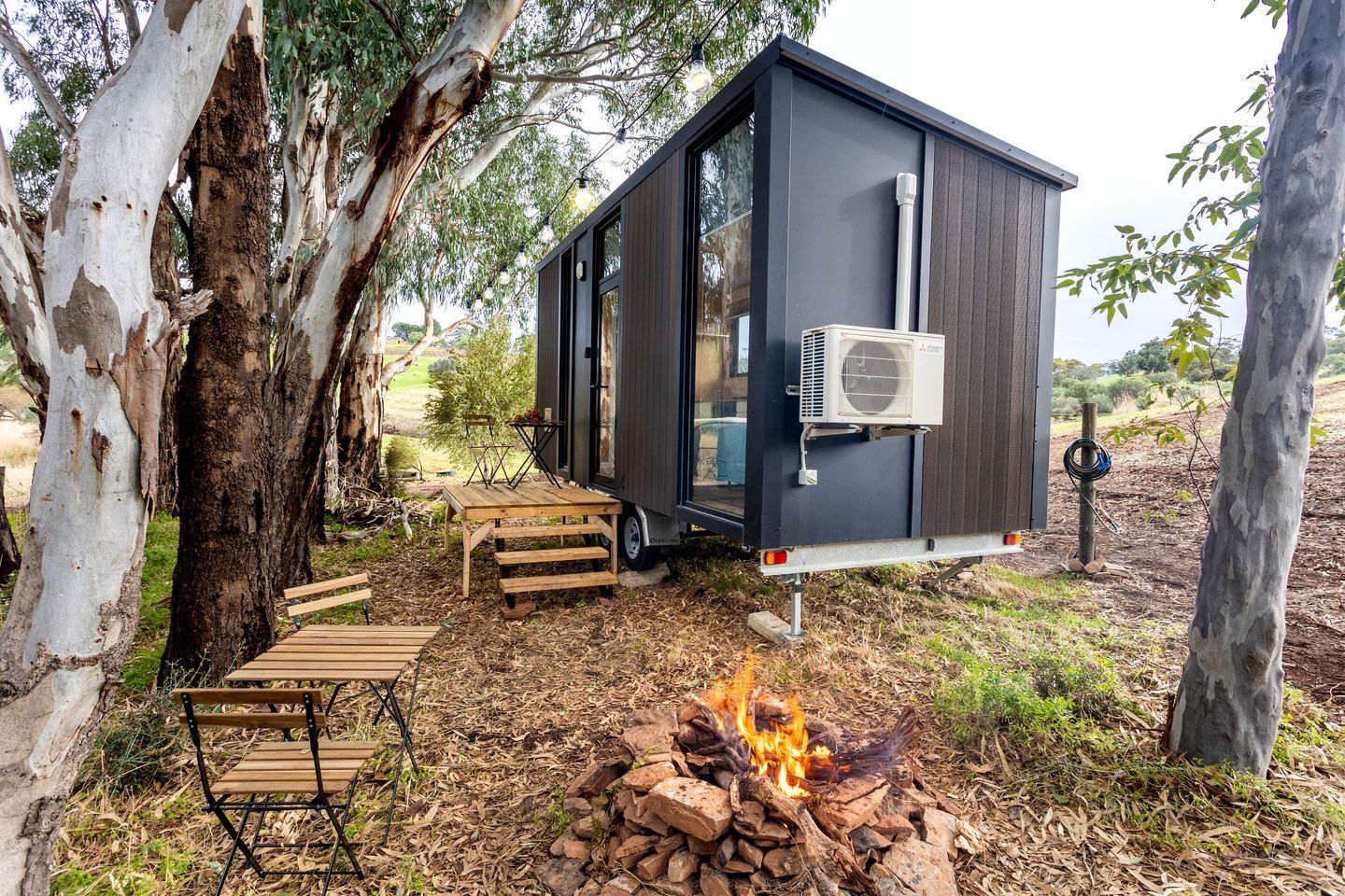 A small, dark-colored mobile home with a fire pit and outdoor furniture.