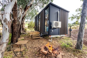 A small, dark-colored mobile home with a fire pit and outdoor furniture.