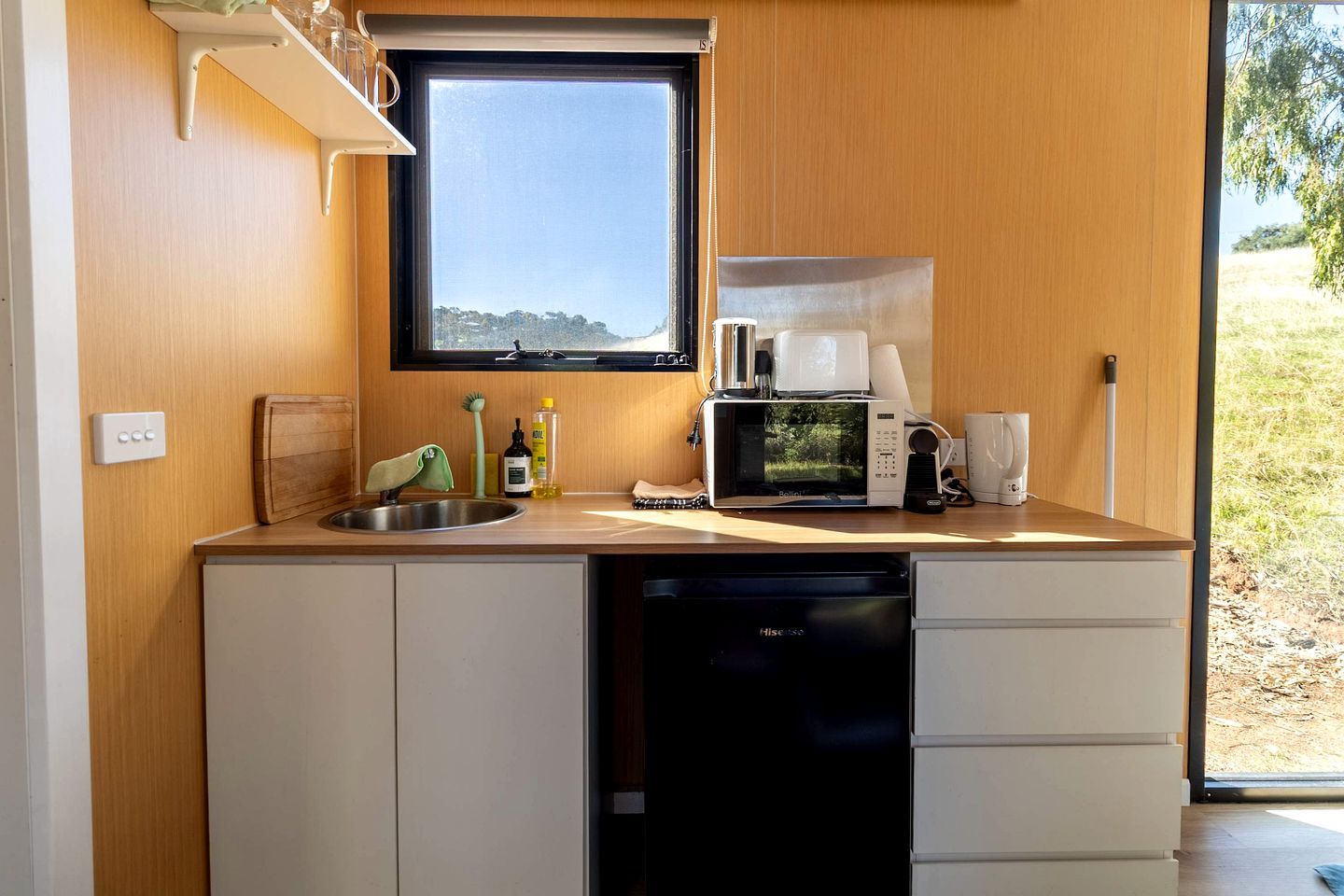 Eine kleine Küche mit Fenster, Spüle, Mikrowelle und Kaffeemaschine.