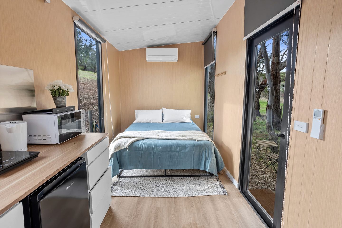 A modern bedroom with a bed, bedside tables, a microwave, and a small table with a plant.