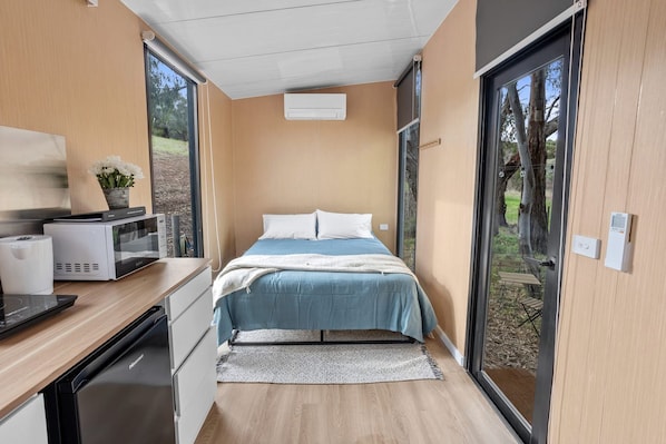 A modern bedroom with a bed, bedside tables, a microwave, and a small table with a plant.