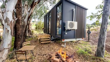A small, dark-colored mobile home with a fire pit and outdoor furniture.