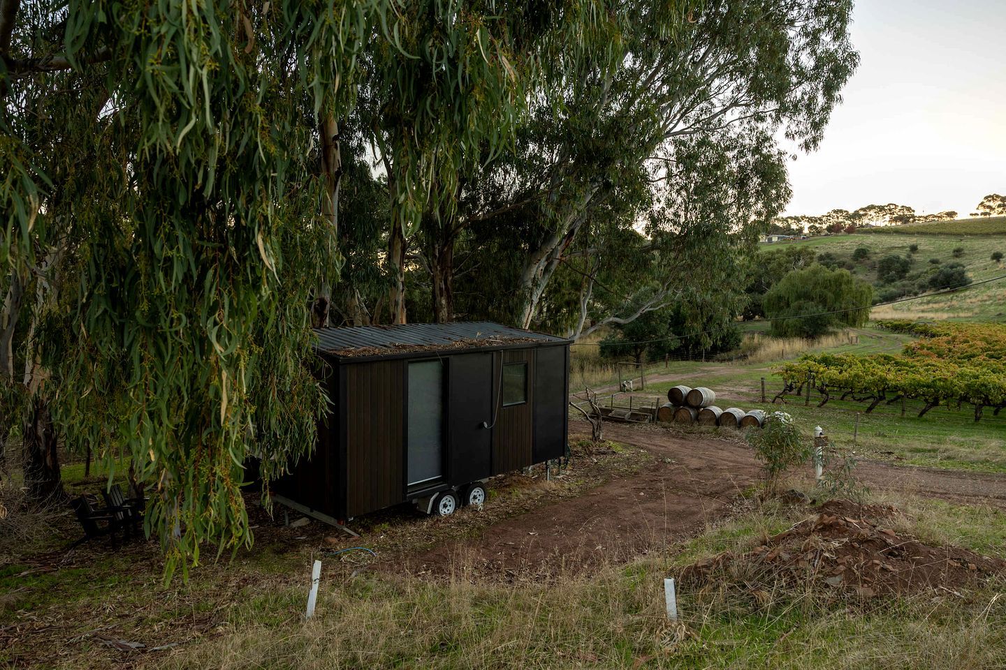 Un petit abri en bois, surmonté d’un toit en métal, situé dans un cadre rural, avec un chemin de terre menant à l’abri.