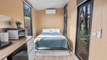 A modern bedroom with a bed, bedside tables, a microwave, and a small table with a plant.