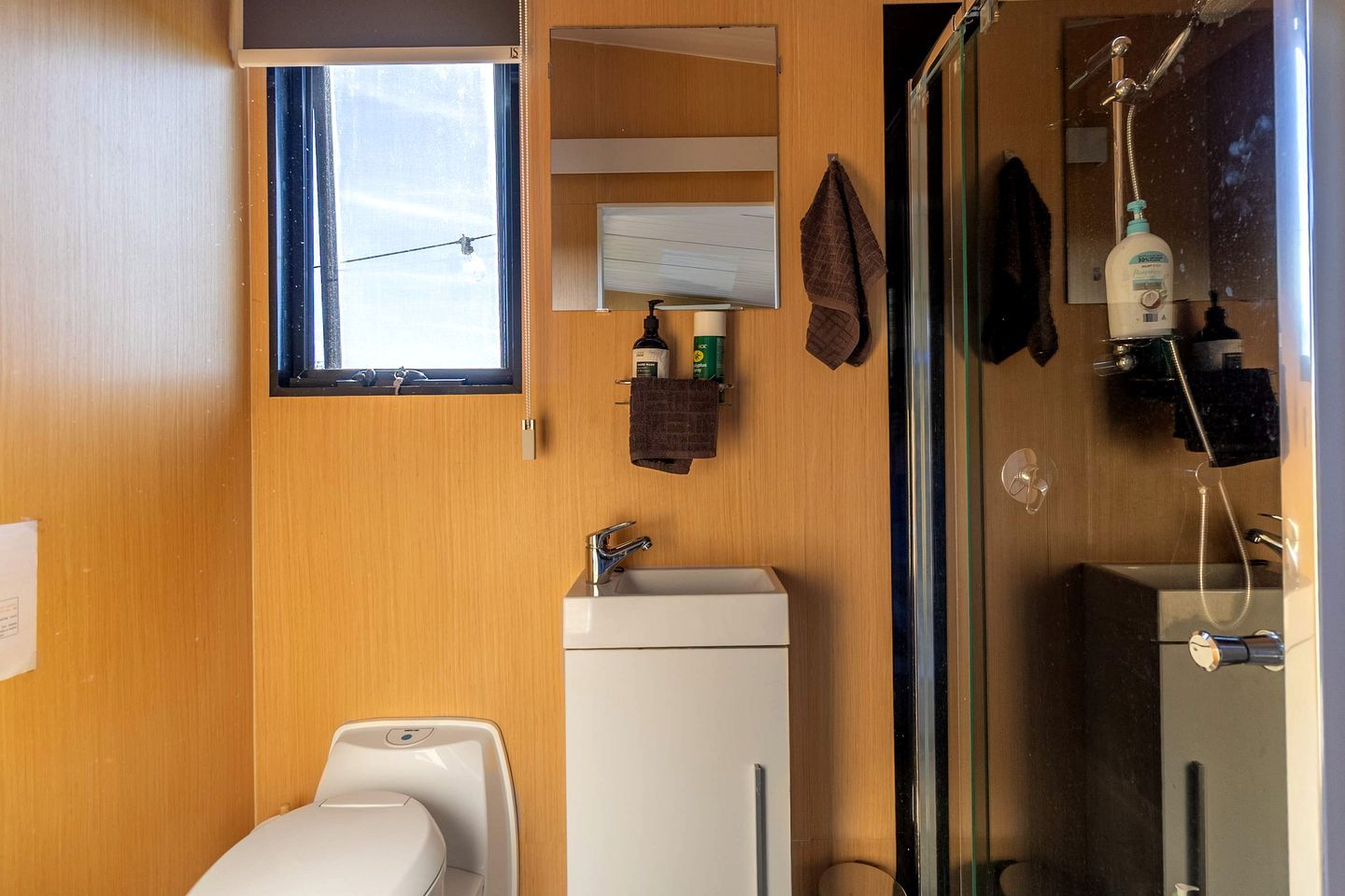 Ein kleines Badezimmer mit Fenster, Waschbecken, Spiegel und Dusche.