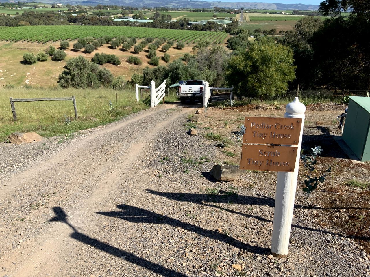Um caminho de cascalho leva a um portão com uma placa indicando 'Peddlar Creek Tiny House' e 'Scrub Tiny House'.