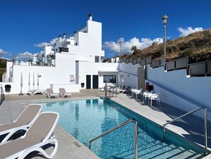 A pool area with lounge chairs, a pool, and a white building with multiple balconies. - Holiday Home in Nerja With Sea Views (Nerja)