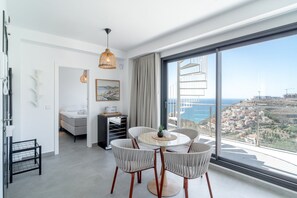 A modern hotel room with a balcony, a dining area with wicker chairs, and a large window offering a city view. - Holiday Home in Nerja With Sea Views (Nerja)