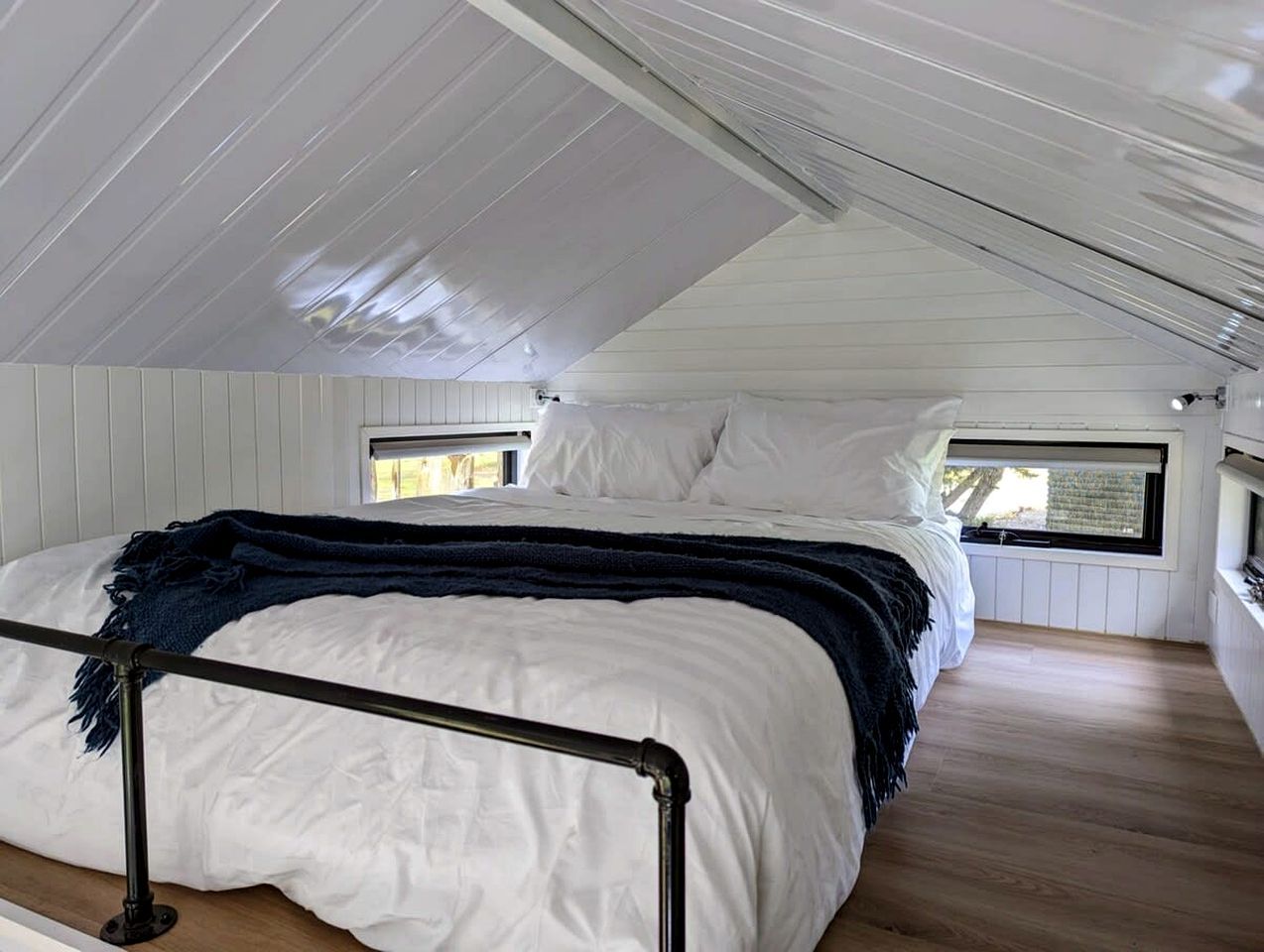 A single bed with a headboard, white bedding, and a dark blue throw blanket. There is a window on the right side of the bed.