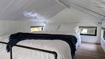 A single bed with a headboard, white bedding, and a dark blue throw blanket. There is a window on the right side of the bed.