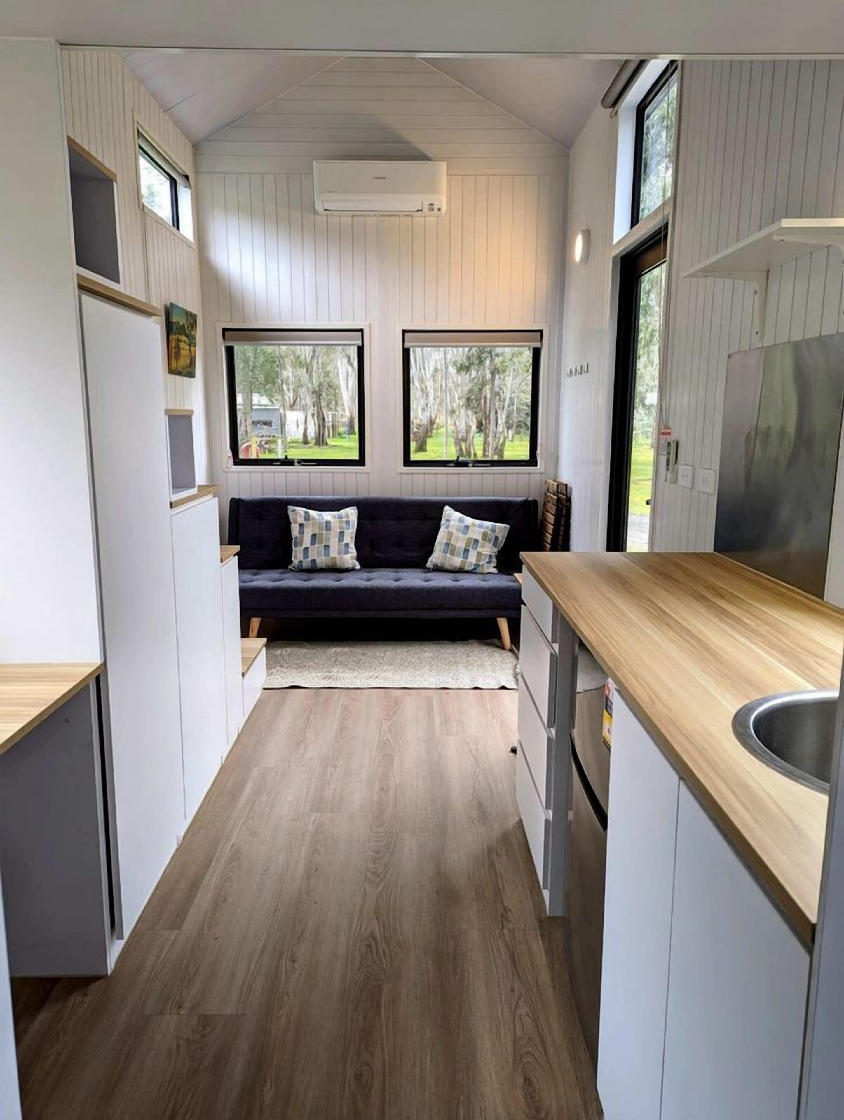 Une cuisine compacte dotée d’un plan de travail en bois, d’une cuisinière intégrée et d’un coin salon avec un canapé foncé.