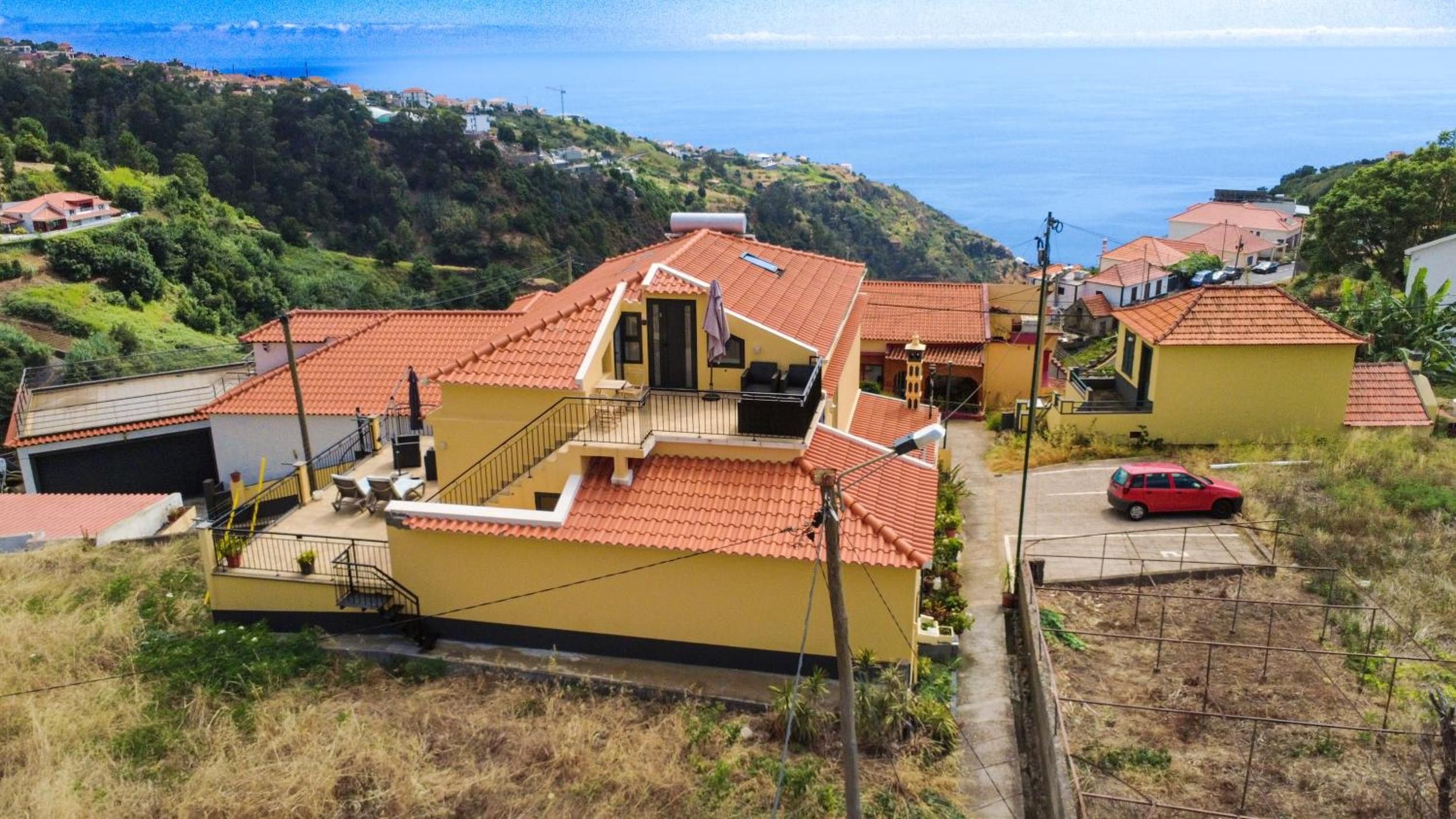 Un bâtiment jaune avec un toit recouvert de tuiles rouges, un balcon et une vue sur la mer.