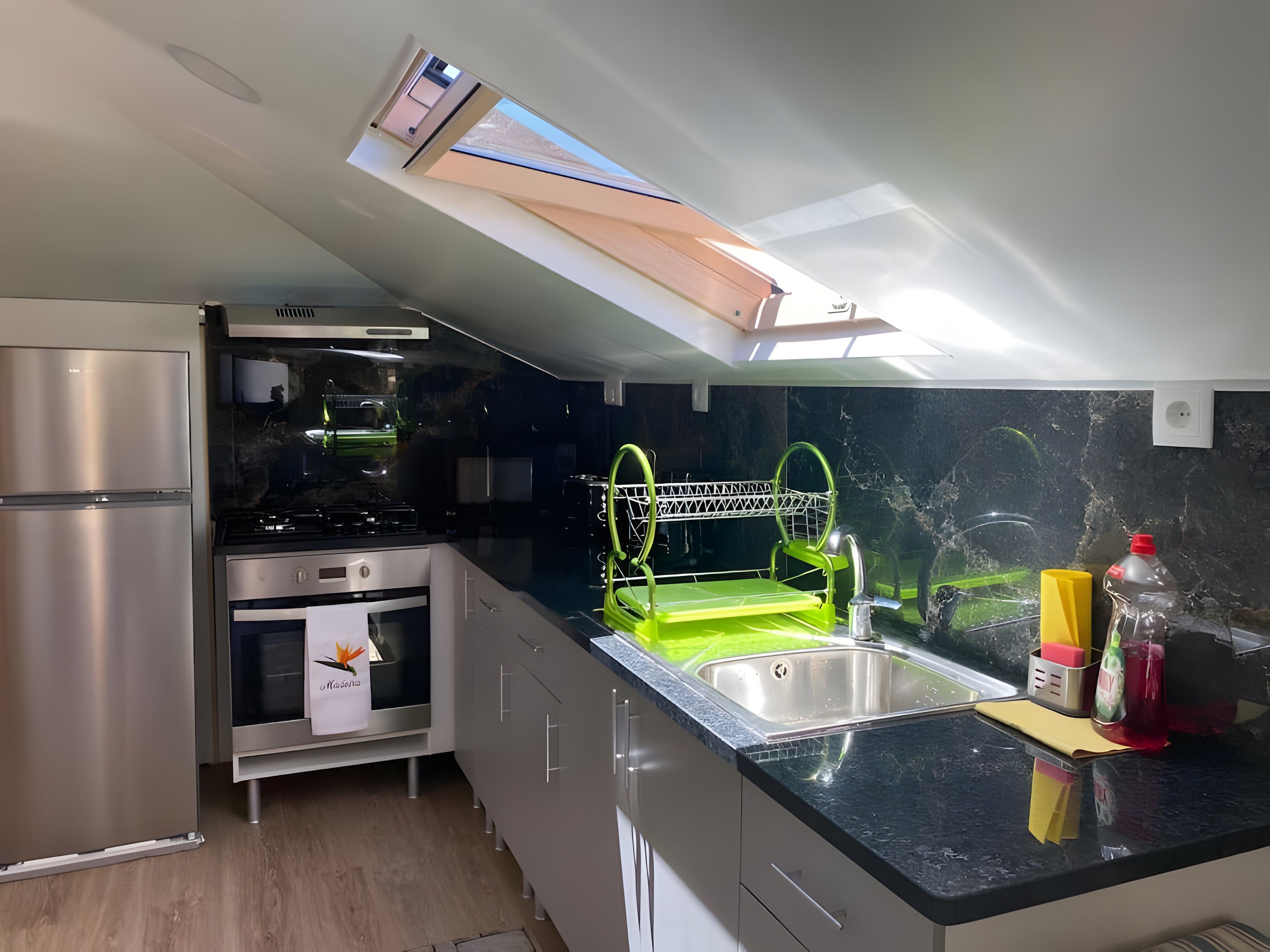 A modern kitchen with a skylight, stainless steel appliances, and a green dish rack.