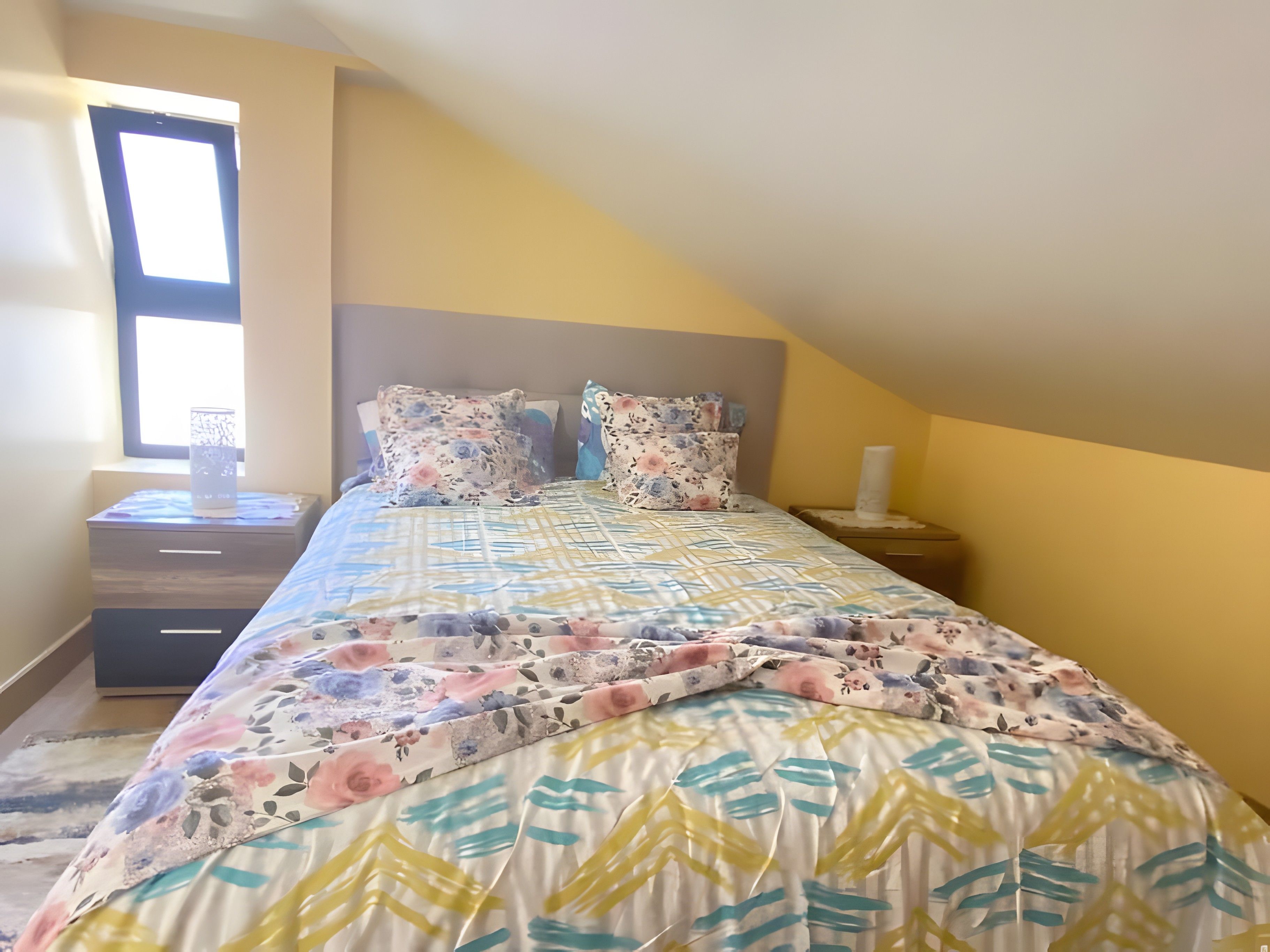 Ein Schlafzimmer mit einem Bett, Nachttischen, einem Fenster und einem Beistelltisch.