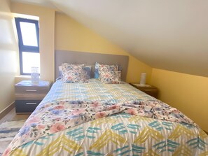 Ein Schlafzimmer mit einem Bett, Nachttischen, einem Fenster und einem Beistelltisch.