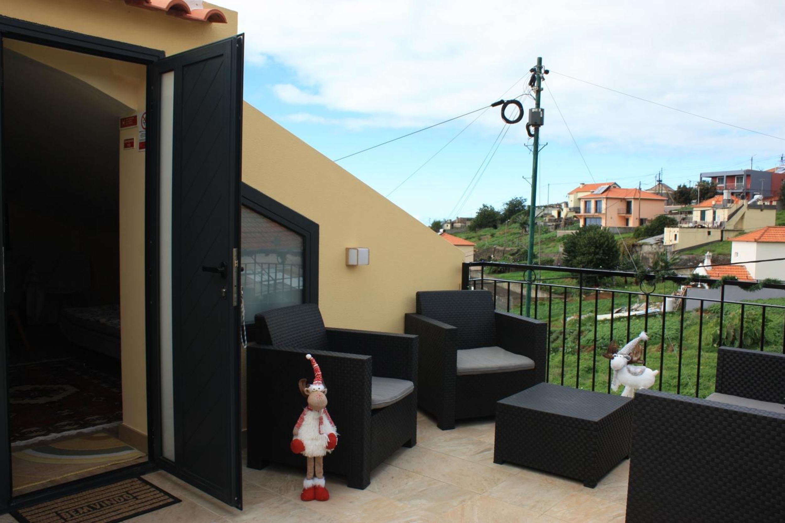 Un balcón abierto con mobiliario exterior, una pequeña figura decorativa y vistas al vecindario.