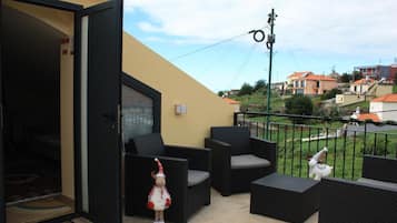 Un balcón abierto con mobiliario exterior, una pequeña figura decorativa y vistas al vecindario.