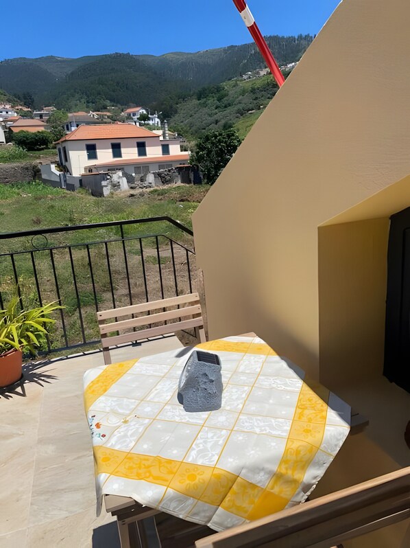 Un balcon avec une table et une chaise, un pot de fleurs et une vue sur une colline parsemée de bâtiments.