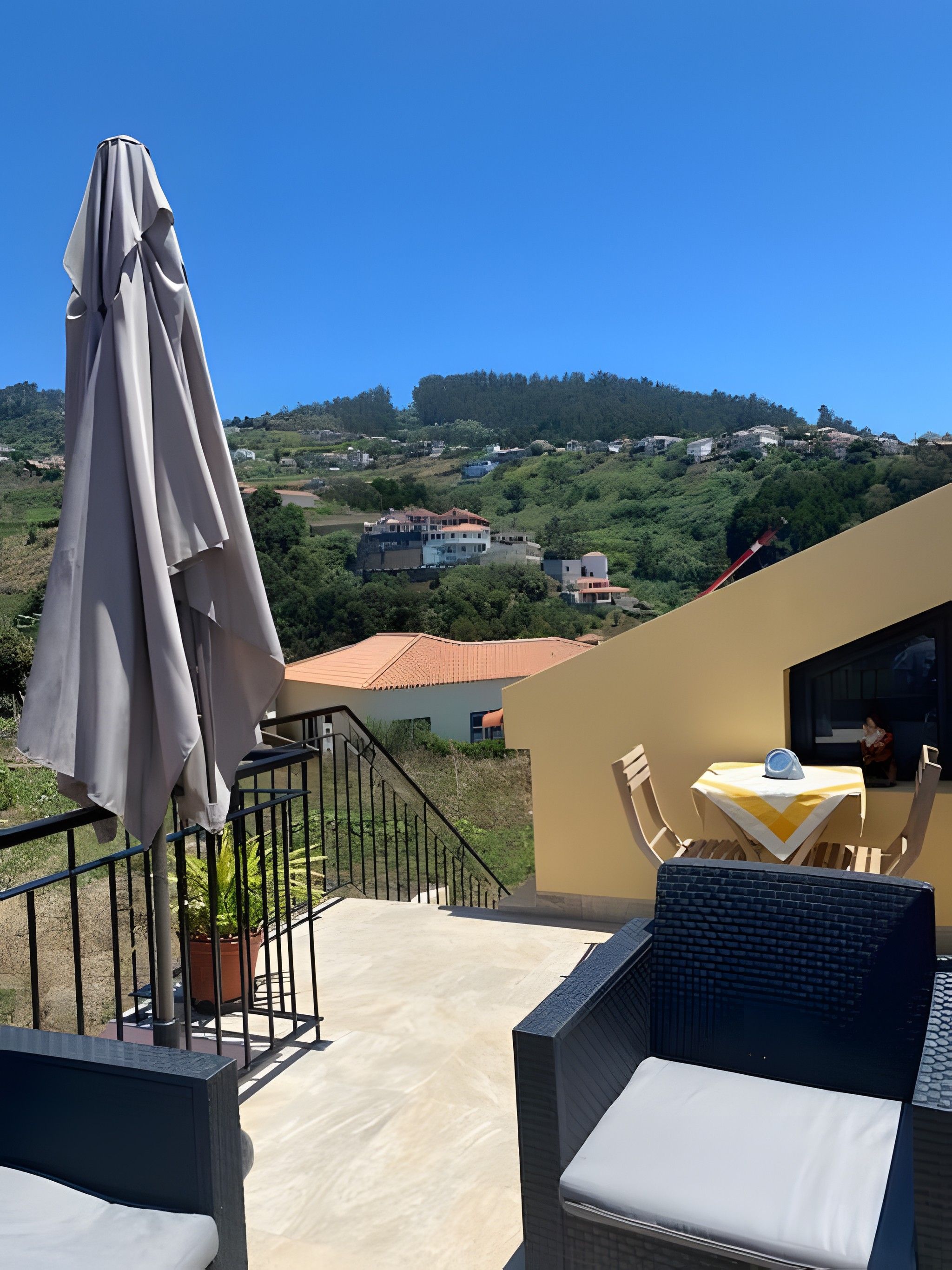 Ein Balkon mit Blick auf eine Hügellandschaft, ein Tisch mit einem Stuhl und ein Blumentopf.