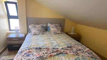 Un dormitorio con una cama, una mesita de noche, una ventana y una mesilla.