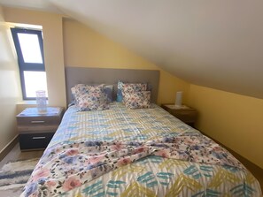 Une chambre à coucher avec un lit, une table de chevet, une fenêtre et une petite table placée près du lit.