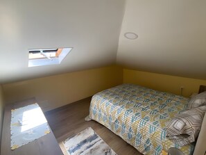 A bedroom with a bed, a small skylight, and a wooden floor. - Apartment 'Casinha Gomes' with Sea View (Calheta)