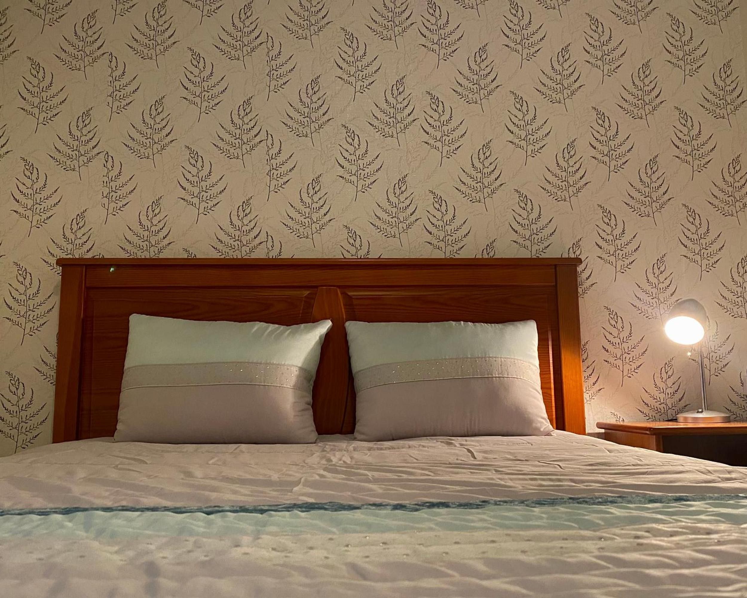Ein Bett mit Holz Kopfteil, zwei Kissen und einer Nachttischlampe.