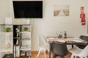 A dining area with a table set for four, a television mounted on the wall, and a bookshelf with various items.