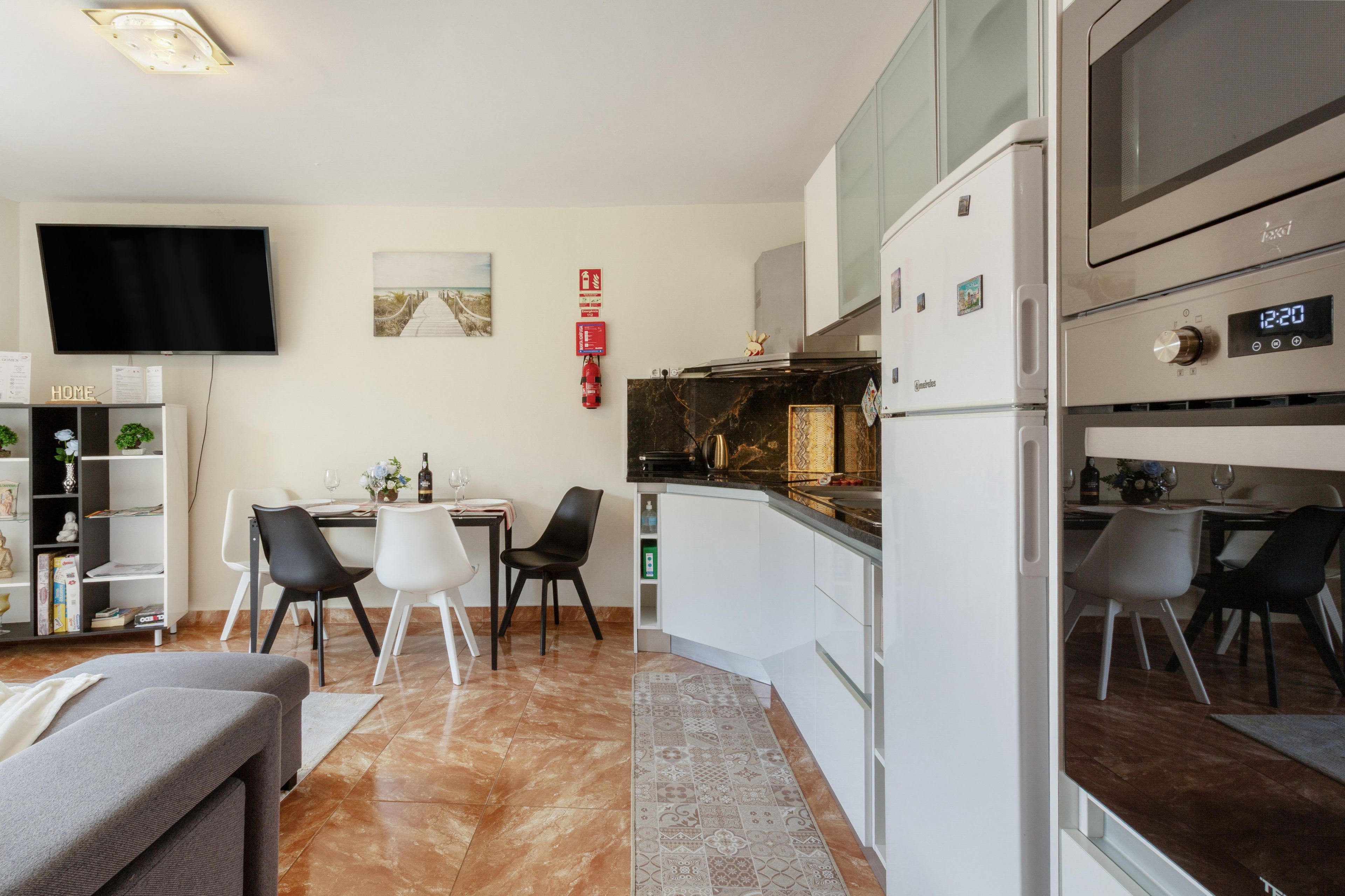 Een moderne keuken met een inbouwoven en magnetron, een eethoek met een tafel en stoelen, en een flatscreen televisie aan de muur bevestigd.