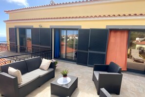 Un balcón con sofá, sillas y una pequeña mesa, con vista a una zona residencial.