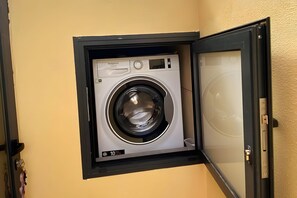 Lavadora compacta, fijada a la pared, en un espacio reducido con panel de control y pantalla digital.