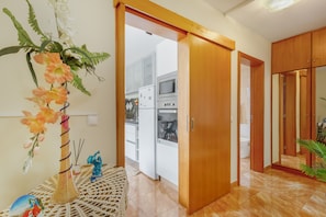 Cuina moderna amb armaris blancs, un frigorífic i una zona de dinar visible a través d'una porta oberta.