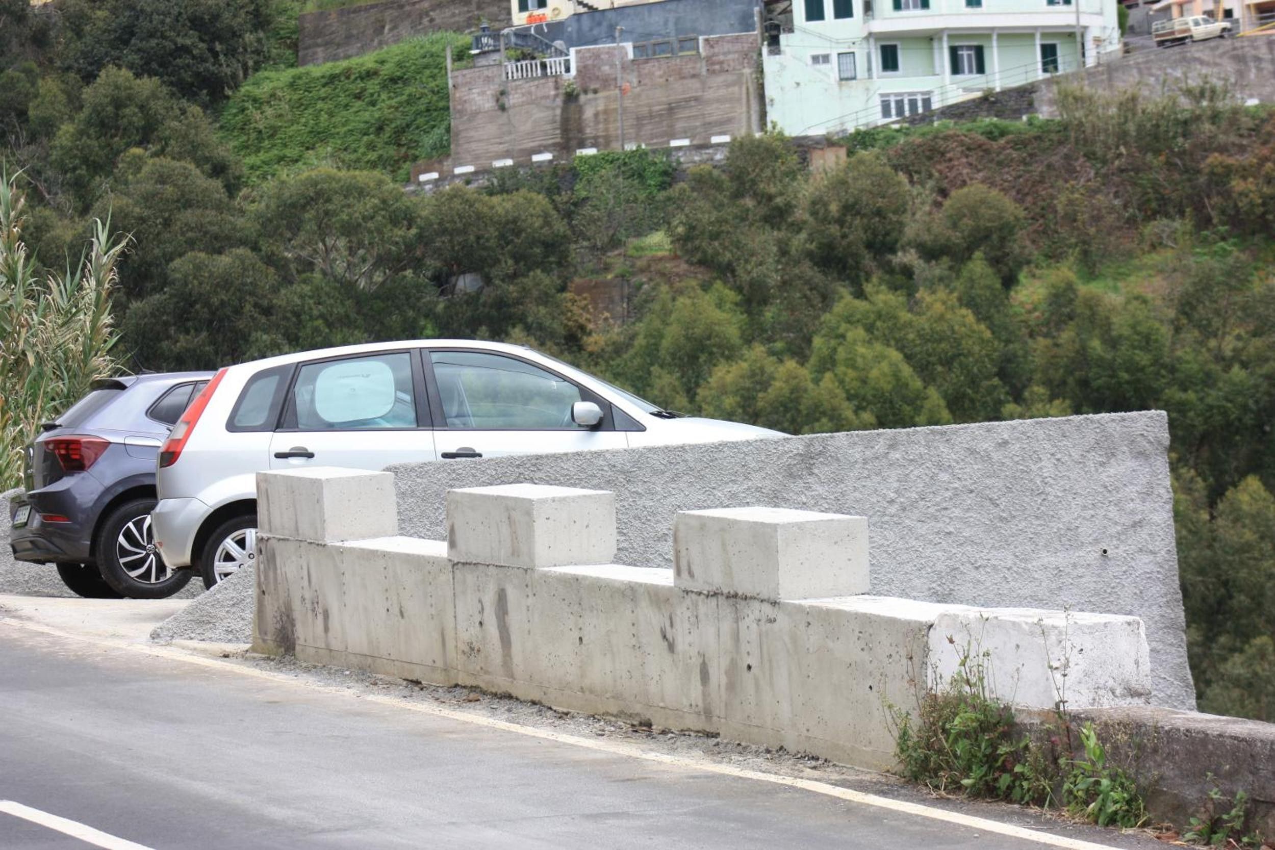 Ein Auto, das neben einer Betonbarriere an einer Straße geparkt ist, mit hügeliger Landschaft im Hintergrund.